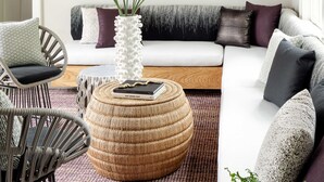 A modern living room with a white sofa, a round woven ottoman, a wicker chair, and a unique ceiling light fixture. - The Richard, The Edgartown Collection (Edgartown)