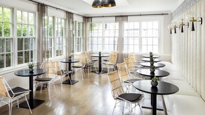 A spacious room with large windows, round tables, wicker chairs, and pendant lighting. - The Richard, The Edgartown Collection (Edgartown)