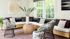 A modern living room with a sectional sofa, two chairs, a coffee table, and a large window with a view of greenery. - The Richard, The Edgartown Collection (Edgartown)