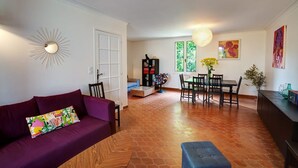 A living room with a purple sofa, a dining table with chairs, a bookshelf, and a large window with greenery outside. - Vacation home in Luberon in the heart of Provence WIFI Free Fiber (Lauris)