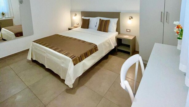 Una habitación de hotel con cama, mesitas de noche, escritorio, silla, armario y lámpara en el techo.