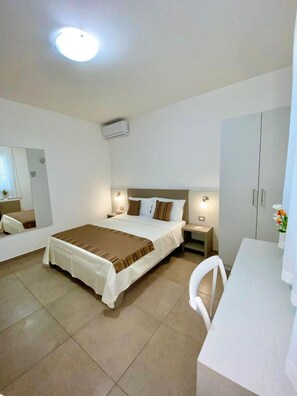 Una habitación de hotel con cama, mesitas de noche, escritorio, silla, armario y lámpara en el techo.