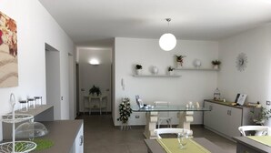 Una cocina moderna con comedor, que incluye una mesa de vidrio, sillas blancas y una lámpara colgante.