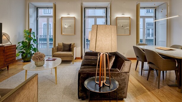 A modern living room with a sofa, a coffee table, a lamp, and a dining area with chairs and a table. - Master Historical Gem in Chiado (Lisboa)