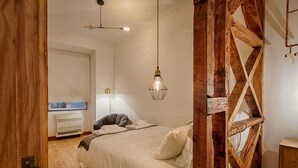 A bedroom with a wooden ceiling structure, a bed with white bedding, a bedside lamp, and a hanging light fixture. - Master Historical Gem in Chiado (Lisboa)