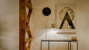 A room with a wooden spiral staircase, a round wall clock, a table with a lamp, and a framed abstract painting. - Master Historical Gem in Chiado (Lisboa)