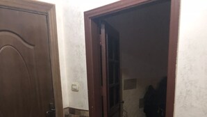 Ein Korridor mit einer geschlossenen Tür links und einer geöffneten Tür rechts, die zu einem Zimmer führt. Der Korridor hat Fliesenboden und eine Wand mit Ziegeln als Akzent.