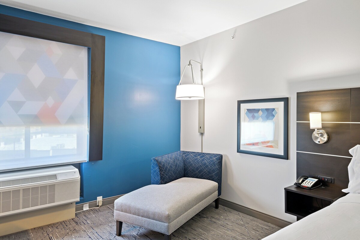 Habitación de hotel con una pared azul decorativa, un pequeño rincón de descanso, una cama, una mesita de noche con teléfono y una lámpara de pared.
