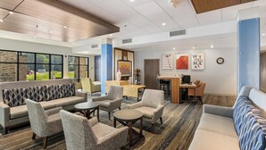 Eine moderne Lobby mit einer Couch, Sesseln, einem Couchtisch und einer Rezeption.