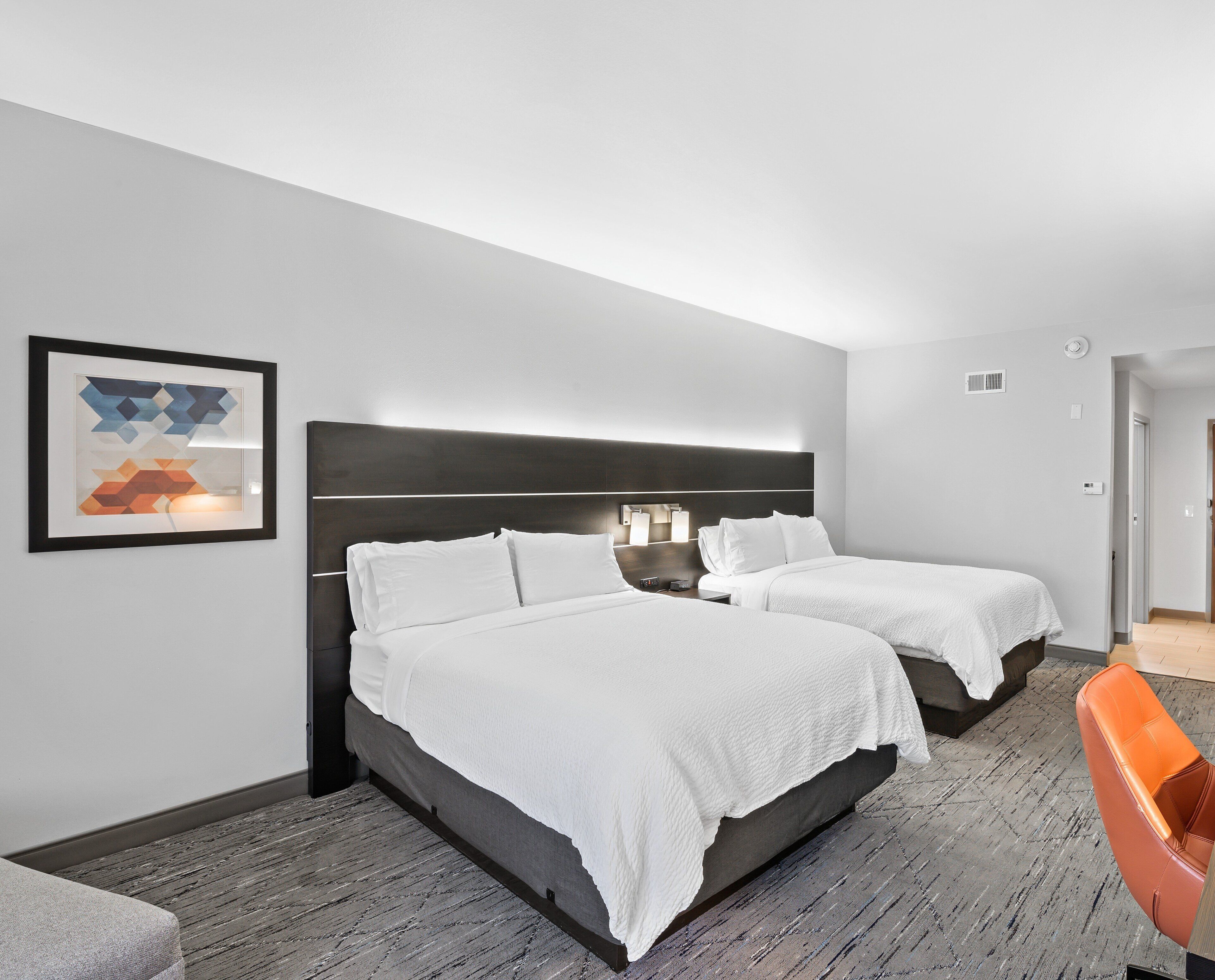 Une chambre d’hôtel avec deux lits, une œuvre d’art abstraite encadrée, une table de chevet et une chaise.