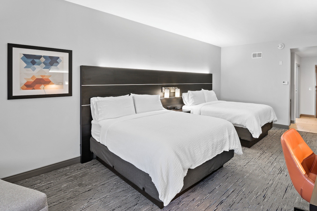 Habitación de hotel con dos camas, una obra de arte abstracta enmarcada, una mesita de noche y una silla.