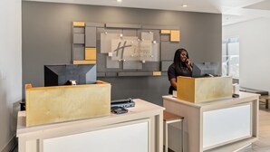 Ein Hotelrezeptionstresen mit modernem Design, ein großes Schild für Holiday Inn Express Suites und eine Rezeptionistin hinter dem Empfangstresen.