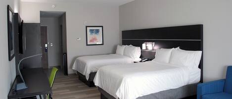 Een hotelkamer met twee bedden, een bureau, een stoel, een televisie en een ingelijste foto aan de muur.