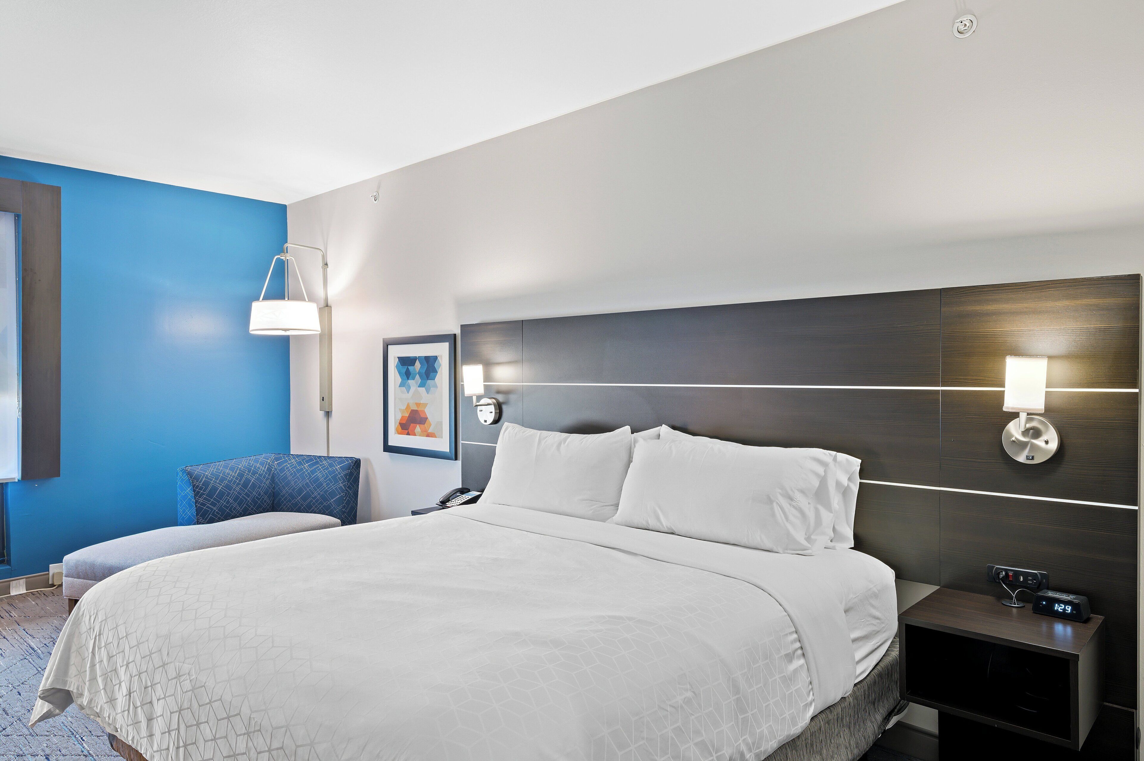 A hotel room with a large bed, a bedside table with a lamp, and a wall-mounted light.
