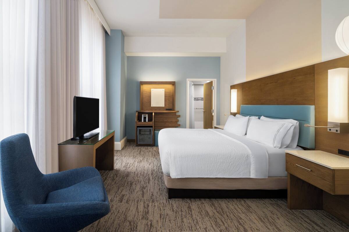 A hotel room with a bed, a TV, a desk, and a chair.