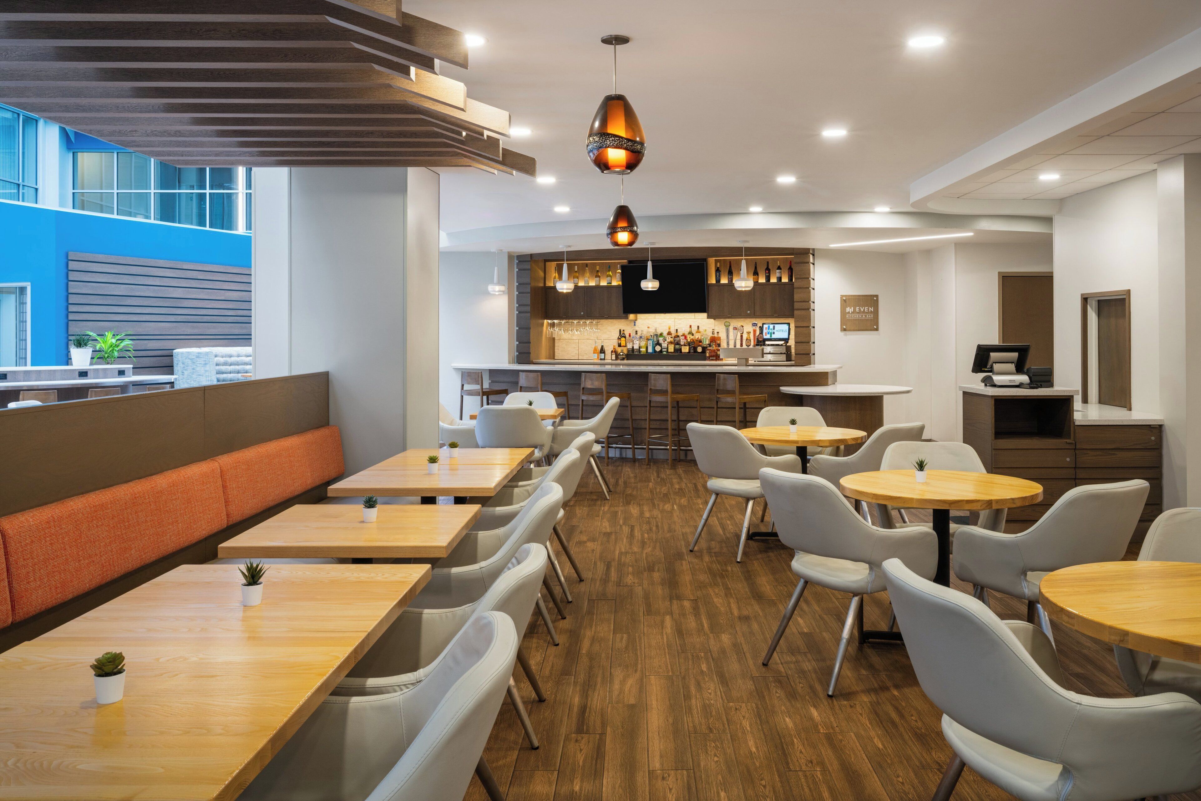 Ein modernes Restaurant mit Holztischen und -stühlen, einer Bar und einer Sitzgruppe mit einer Bank.