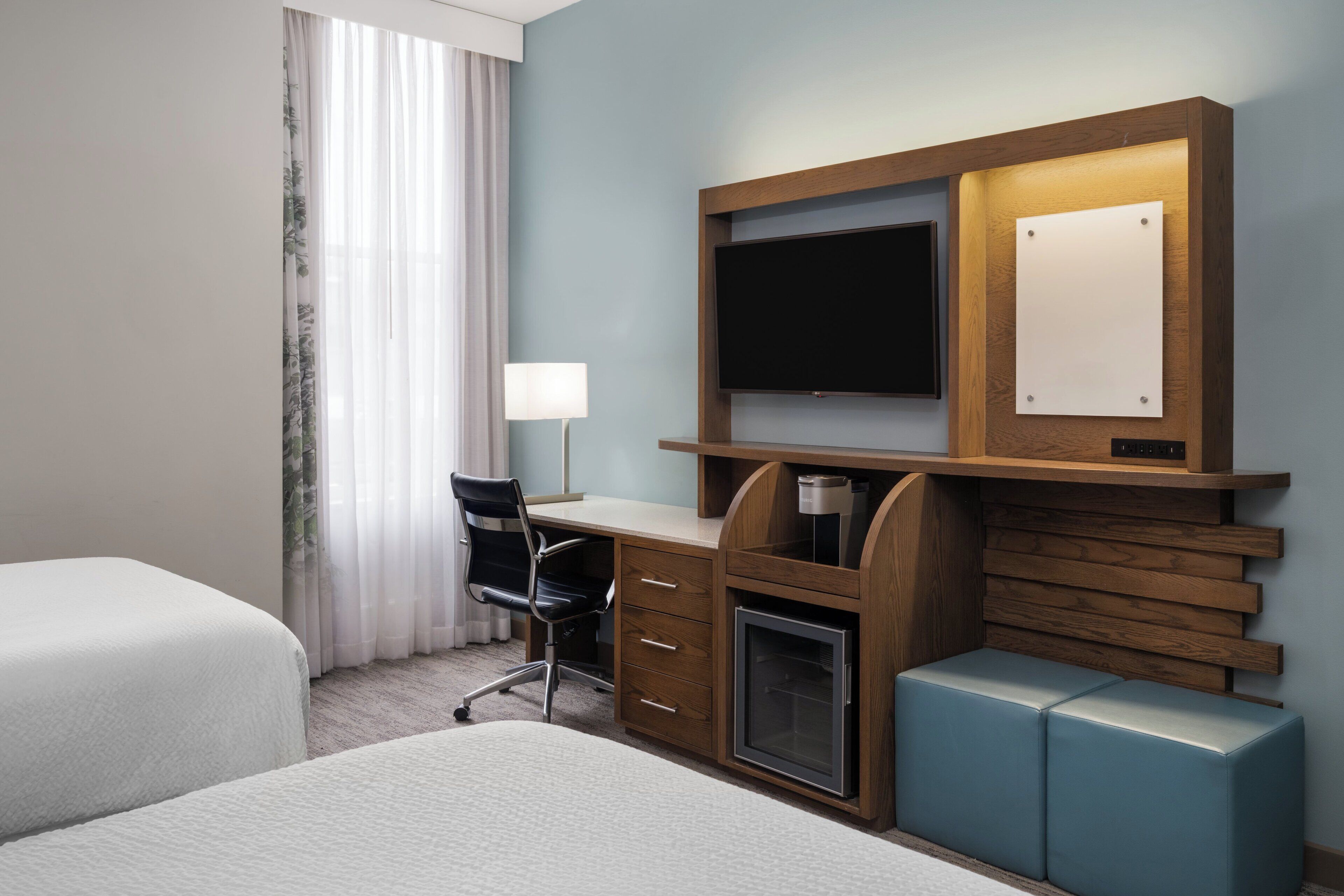 Habitación de hotel con cama, escritorio con computadora, televisión y un pequeño espacio de descanso.