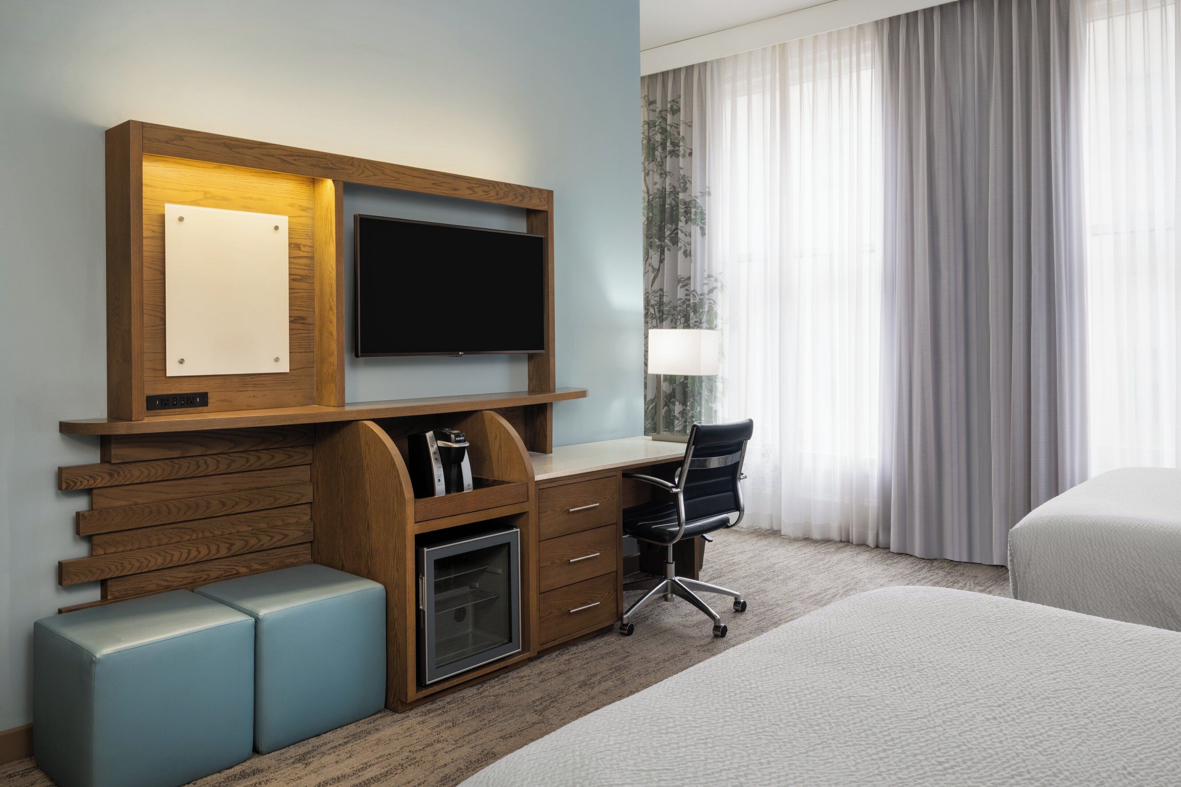 A hotel room with a wooden desk, a flat-screen TV, a chair, a small cabinet, and a bed.