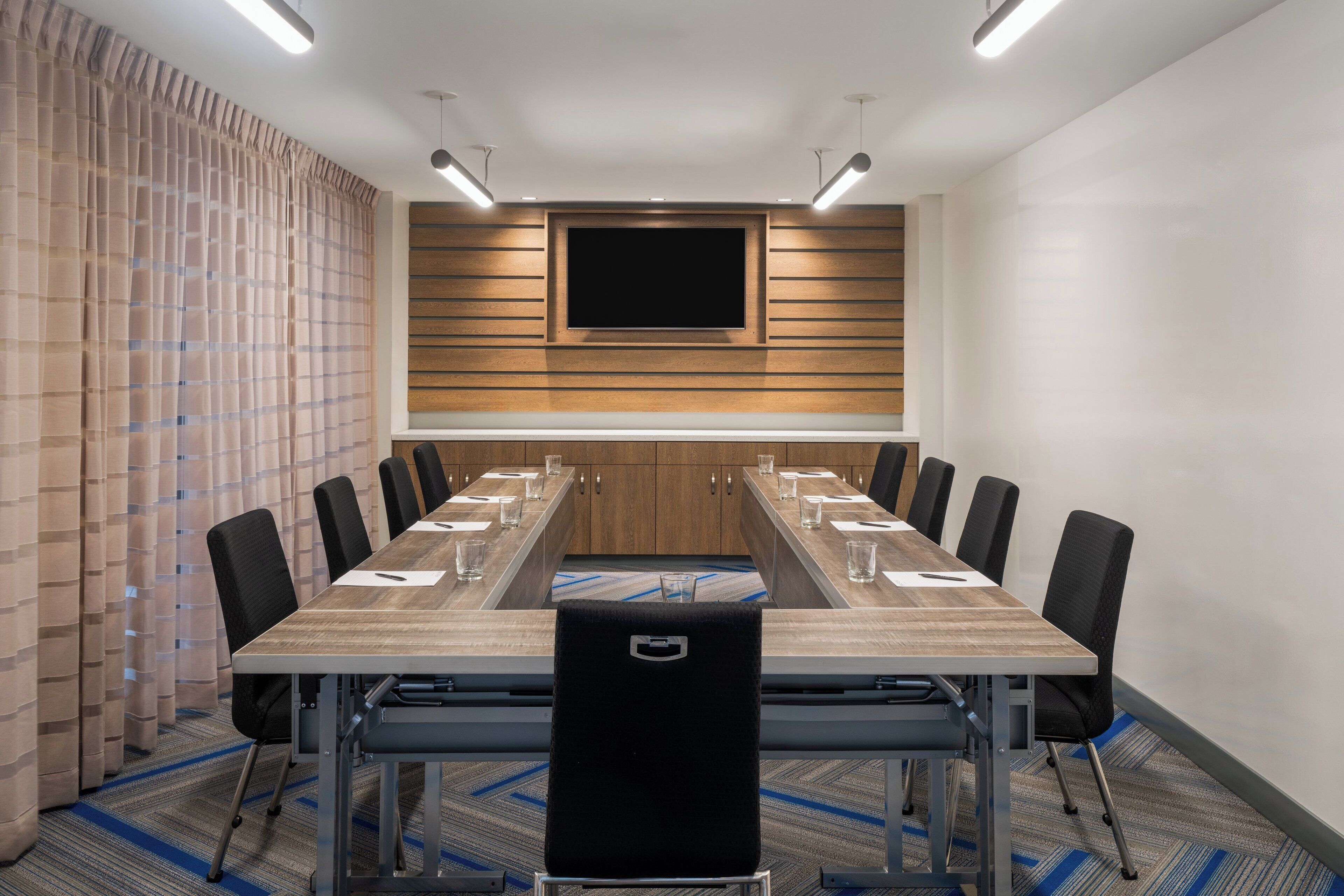 A conference room with a long table, chairs, a flat-screen TV, and wooden panel walls.