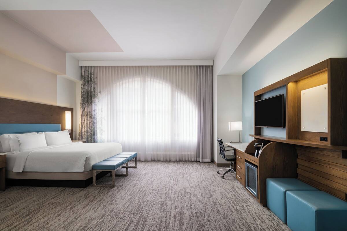 A hotel room with a bed, a desk, a TV, and a seating area.