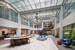 Un hall d’entrée spacieux avec un plafond haut, un espace salon central et un escalier menant aux étages supérieurs.
