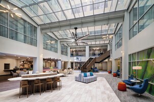 Un hall amplio con techo alto, un área de descanso central y una escalera que sube a los pisos superiores.