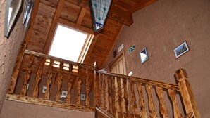 A wooden staircase with a glass balustrade, a door with a number sign, and framed pictures on the wall. - El Trasgu de Foncebadón (Santa Colomba de Somoza)