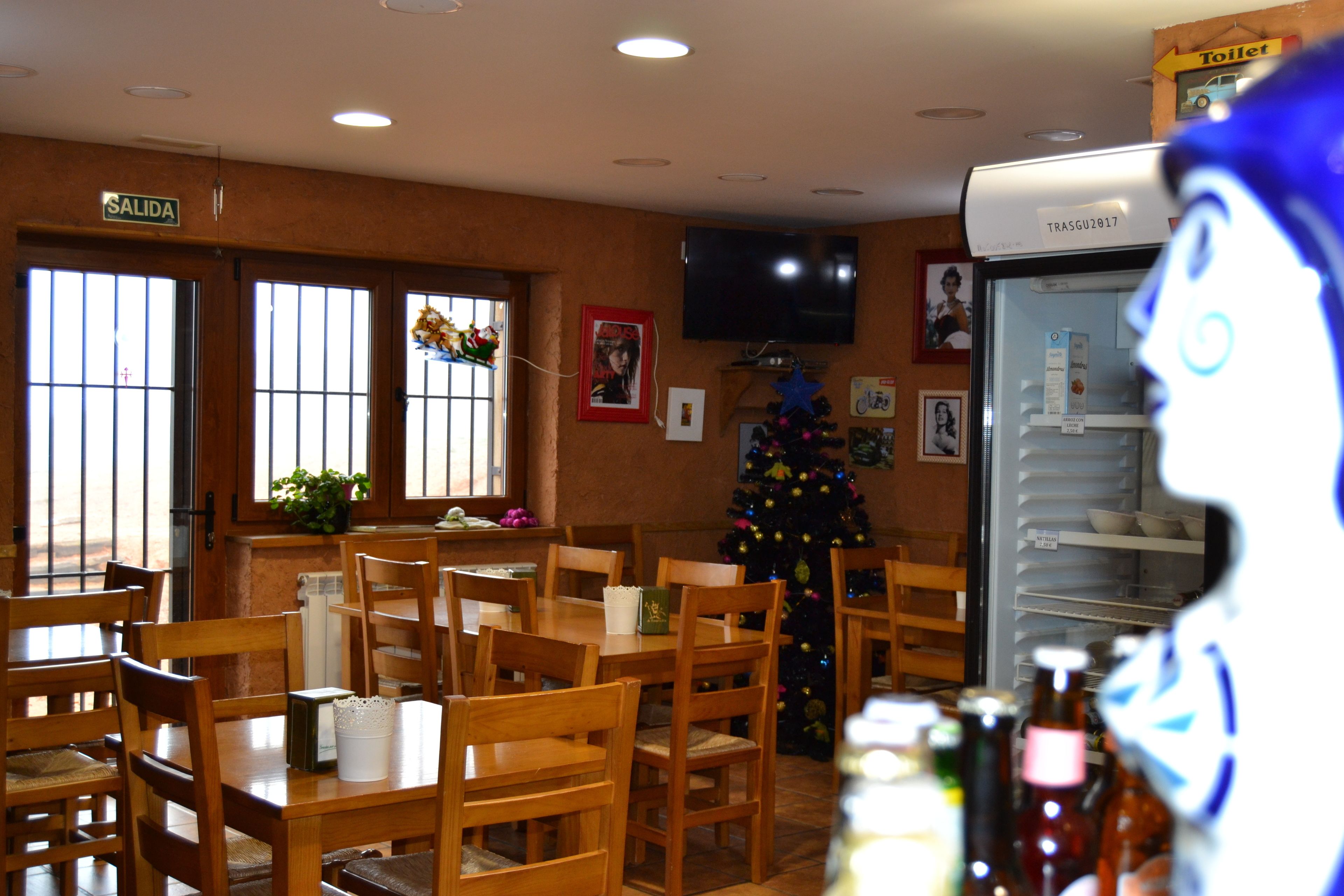 Un restaurante con mesas y sillas de madera, un árbol de Navidad y un refrigerador con un cartel que dice 