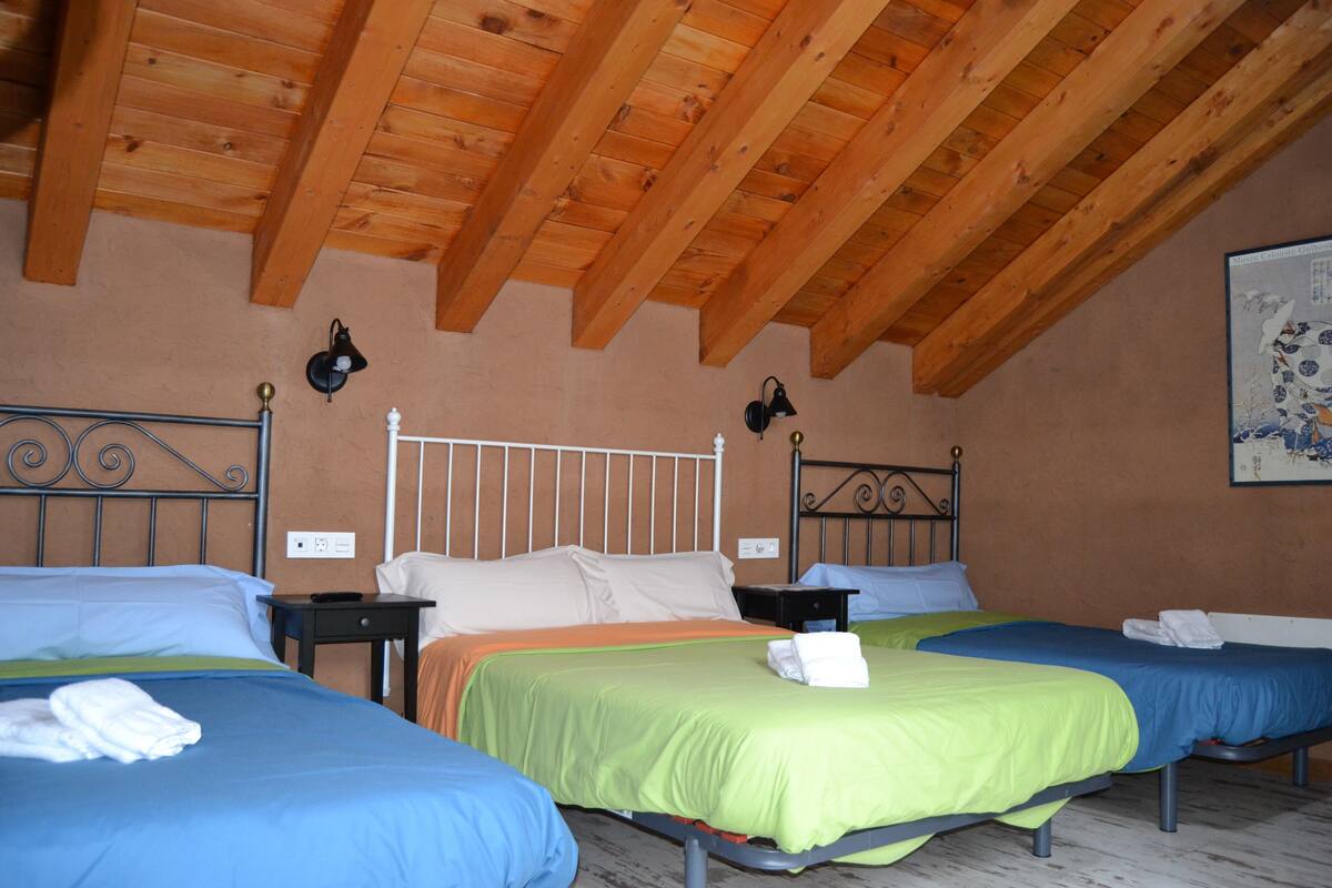 A room with two beds, wooden ceiling beams, and a single wall-mounted light fixture.