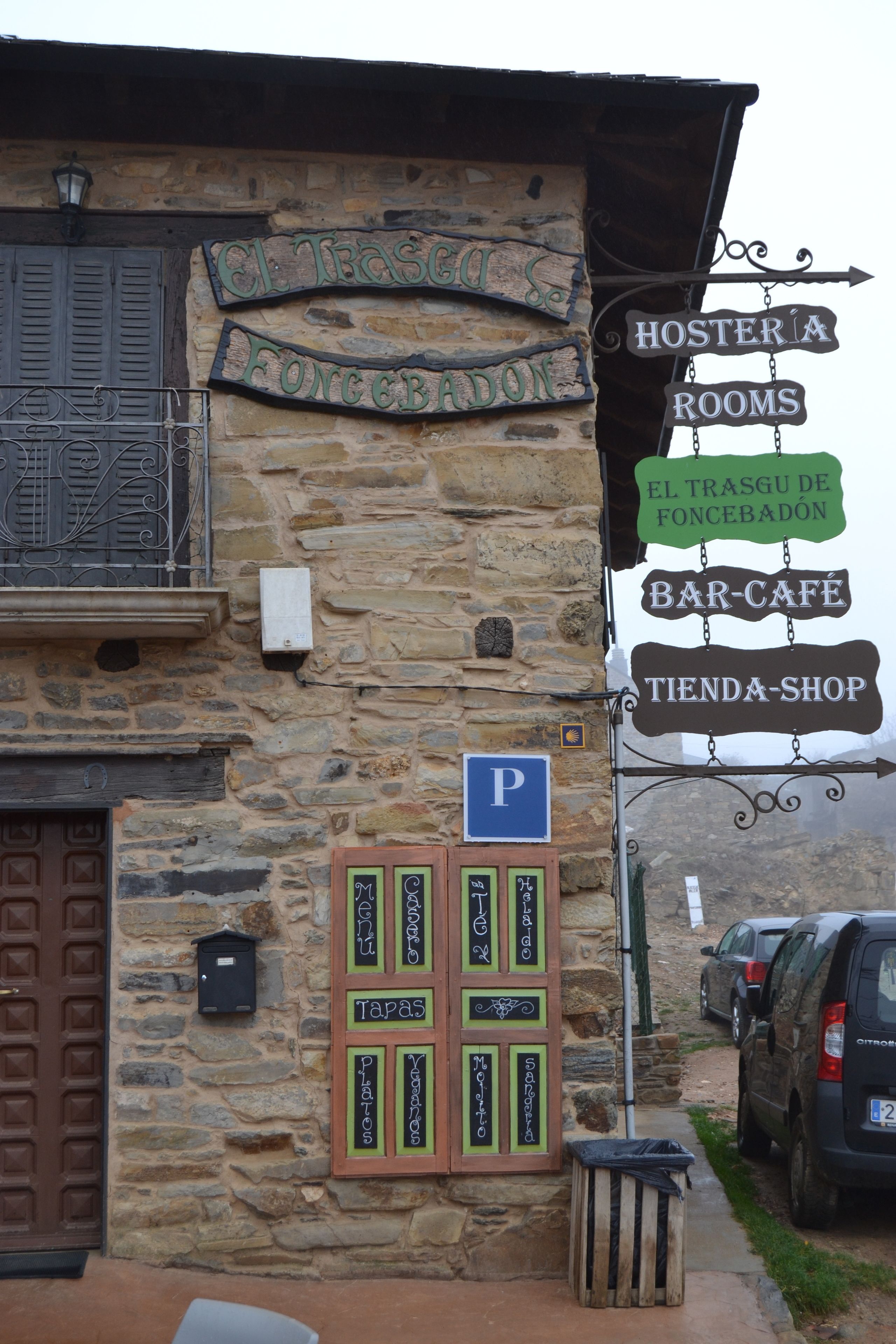 A stone building with a sign indicating 'Hostería Rooms' and 'El Trásgu de Foncebadón Bar-Cafe'.