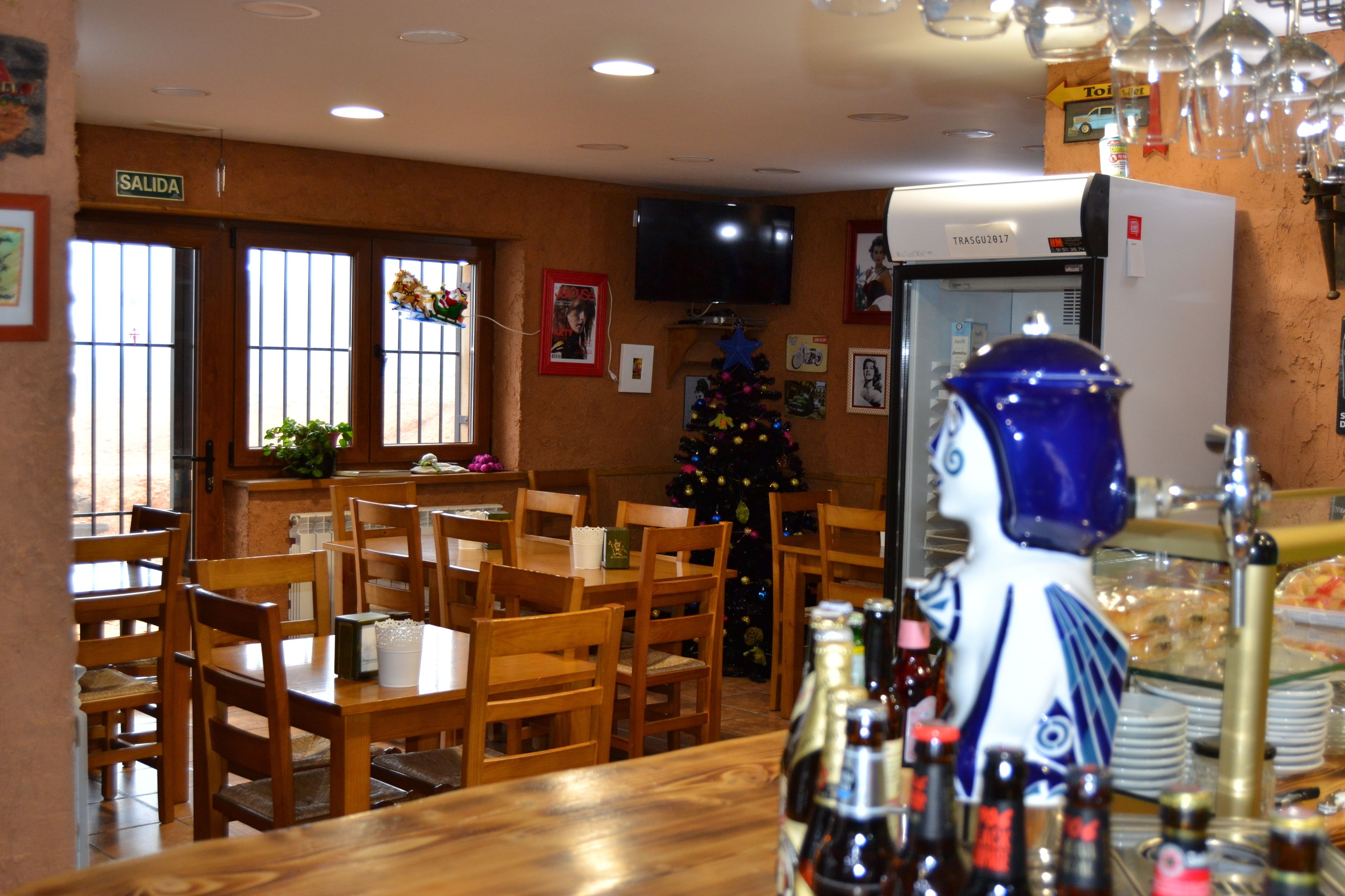 Un restaurante con mesas y sillas de madera, un árbol de Navidad, un televisor en la pared y un refrigerador.