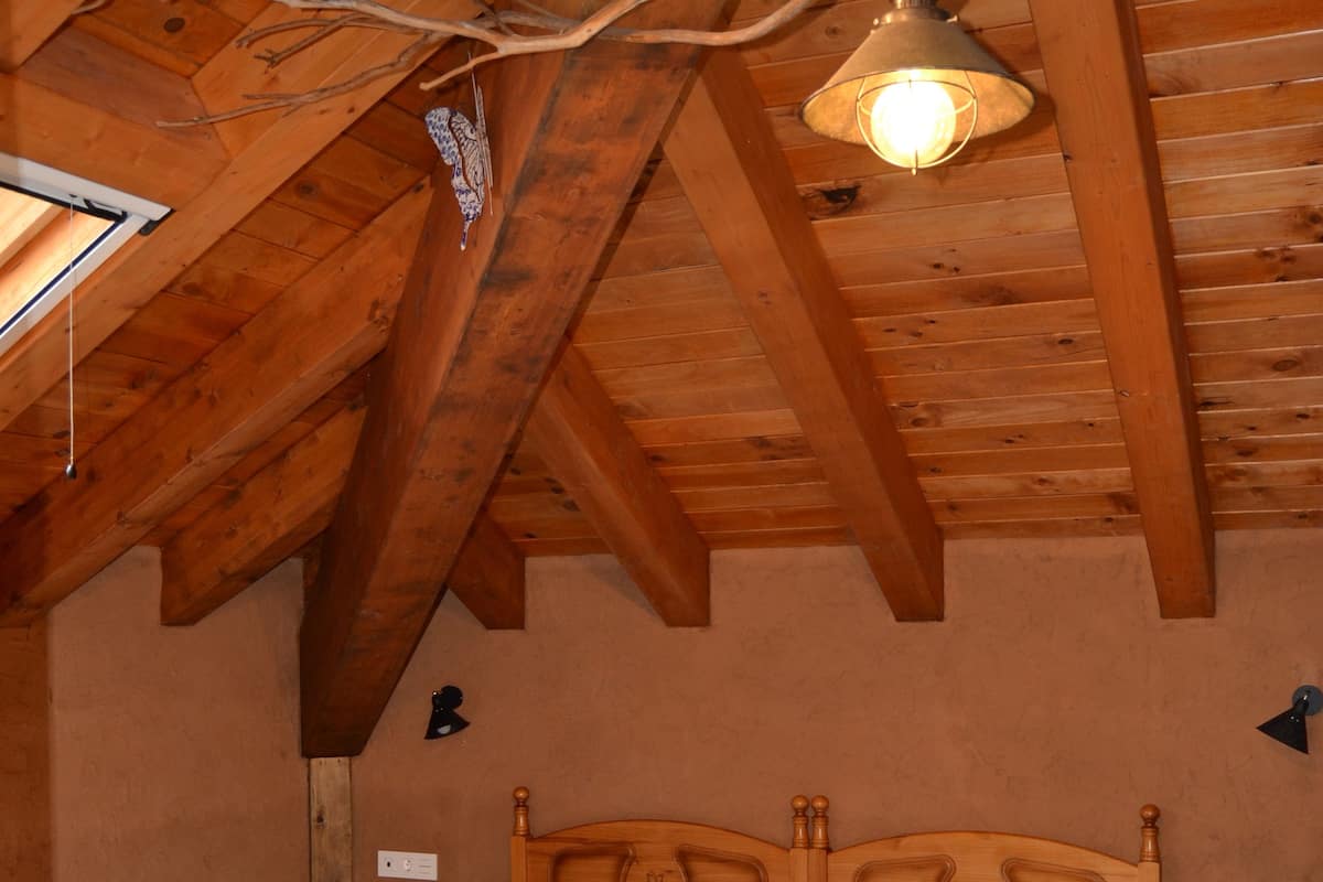 A bedroom with two beds, wooden ceiling beams, and hanging light fixtures.