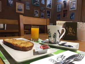 A breakfast setting with toast, a glass of orange juice, a mug with a design, and a book on the table. - El Trasgu de Foncebadón (Santa Colomba de Somoza)