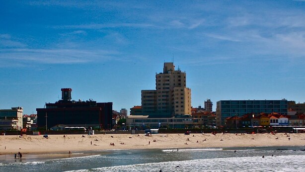 A beach with a tall building in the background, sandy shore, and clear blue sky. - 2 bedroom house with modern furniture1 suite with toillet, terrace /25 km Porto (Cedofeita)