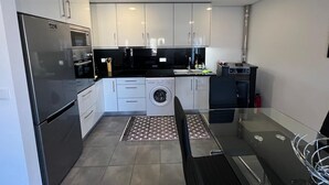 A modern kitchen with white cabinets, a stainless steel refrigerator, a washing machine, and a dining area with a glass table and chairs. - 2 bedroom house with modern furniture1 suite with toillet, terrace /25 km Porto (Cedofeita)