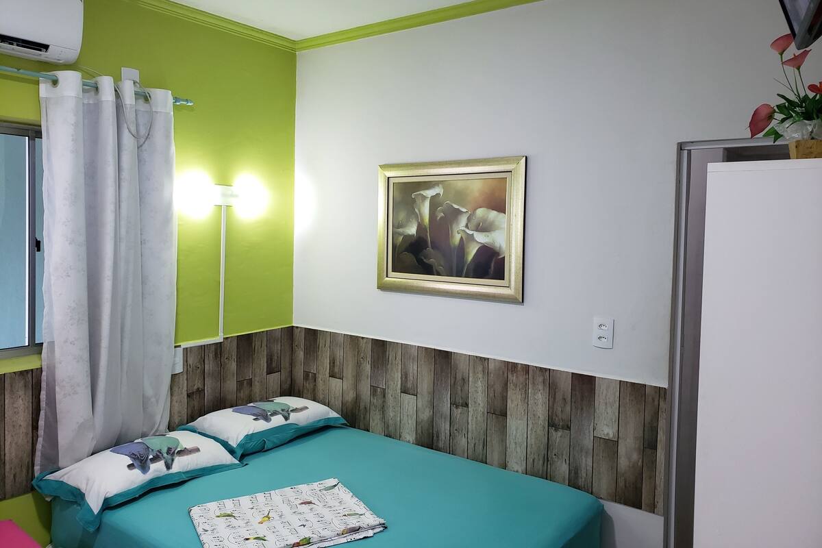 Ein Zimmer mit einem Bett, einem Gemälde, einer Wandklimaanlage und einem Vorhang.