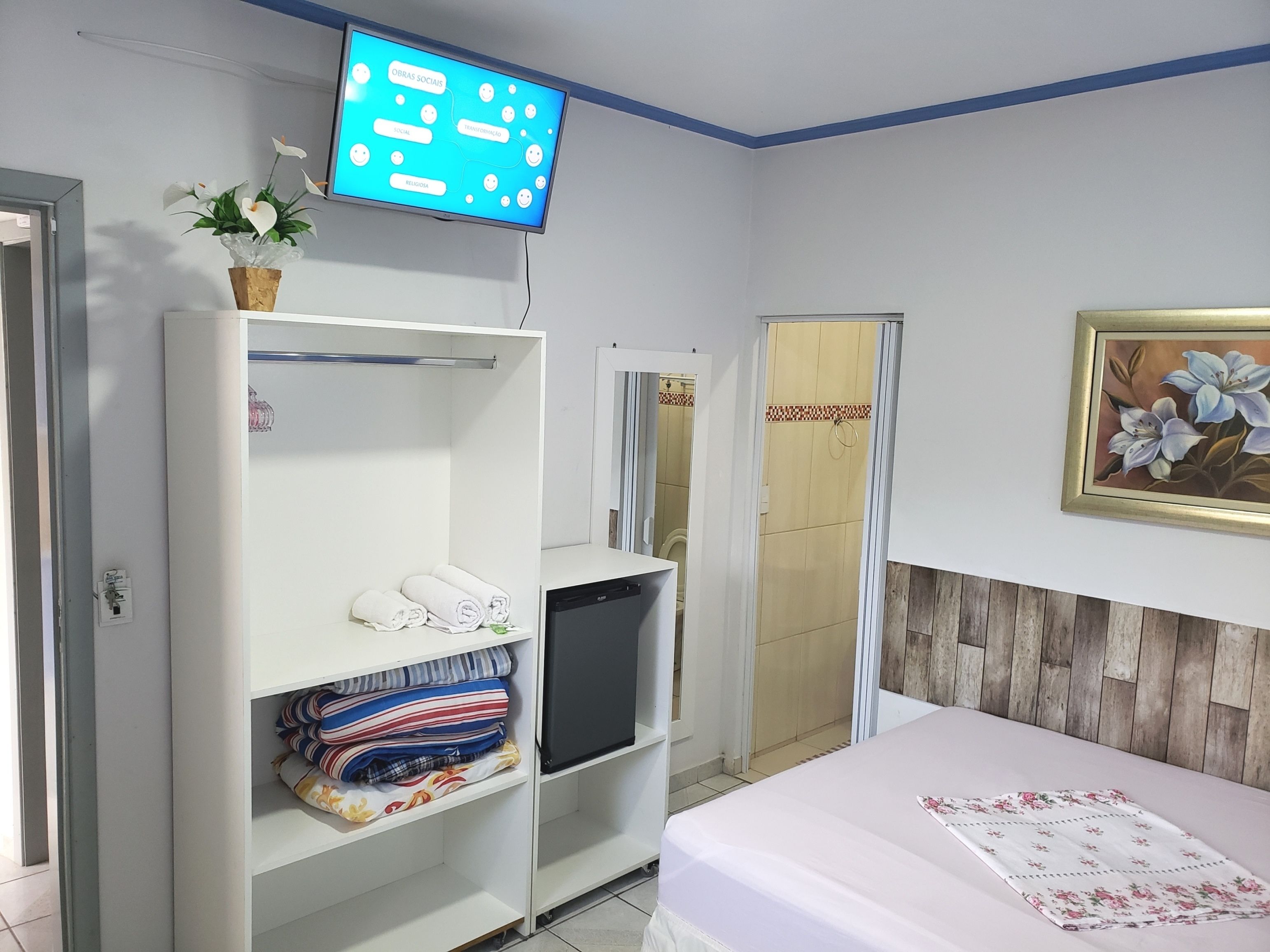 A hotel room with a bed, a TV mounted on the wall, a wardrobe, and a painting on the wall.