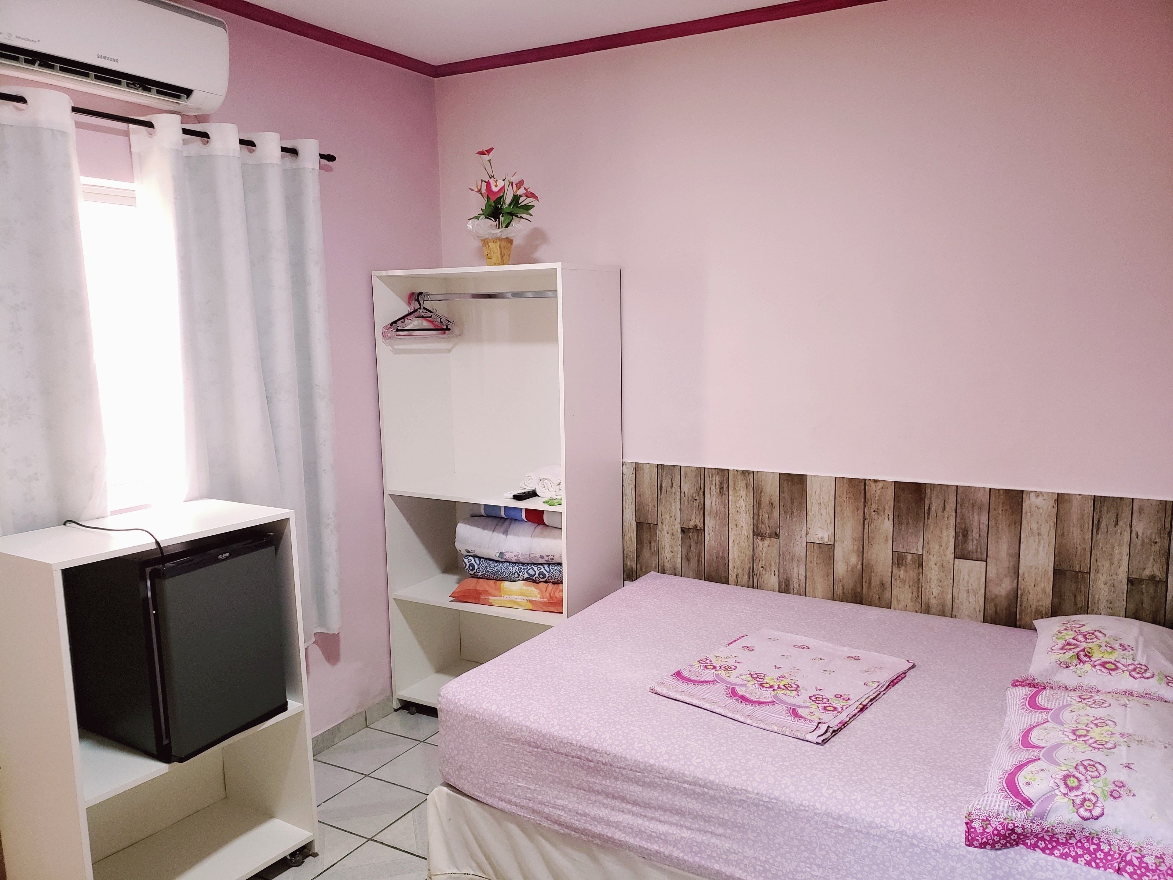 A bedroom with a bed, a wardrobe, a TV, and a window with curtains.