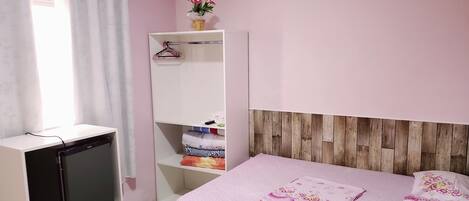 Un dormitorio con cama, armario, televisor y ventana con cortinas.