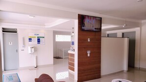 Un espace d’accueil moderne avec un comptoir de réception en bois, un téléviseur fixé au mur et un espace d’attente comprenant un canapé marron et une petite table ronde.