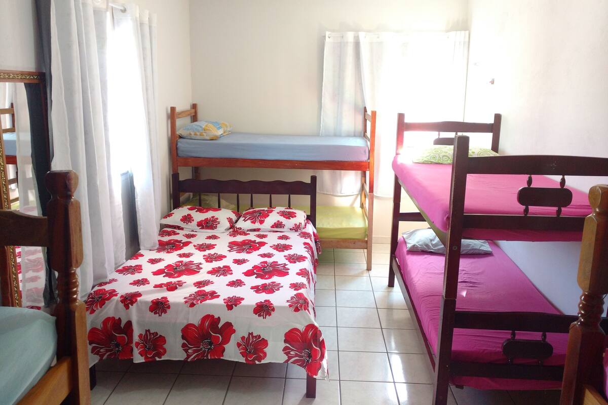Ein Schlafsaalzimmer mit Etagenbetten, einem Einzelbett mit Blumenmuster und einem Stuhl.