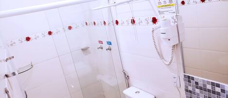 A bathroom with a glass shower enclosure, a toilet, a sink with a soap dispenser, and a hand dryer.