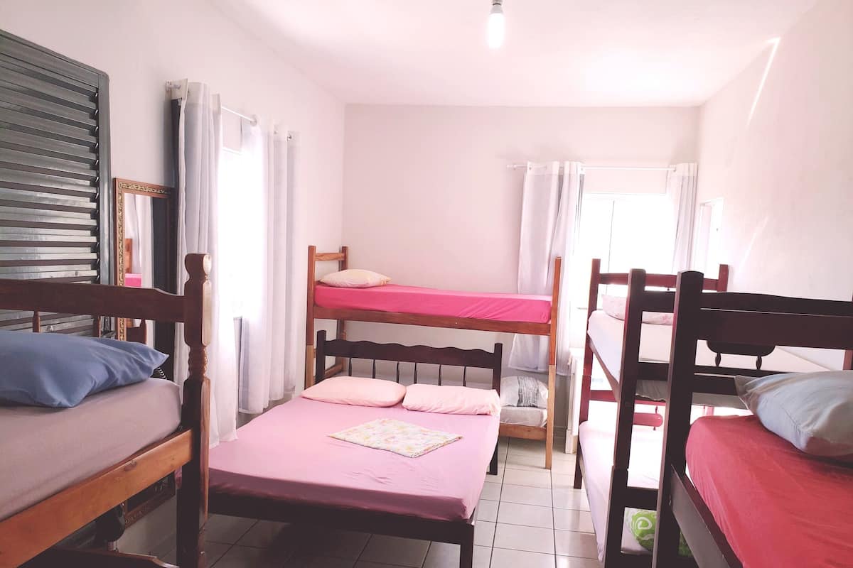 Ein Schlafsaalzimmer mit Etagenbetten, einem Holz-Kopfteil, einem Spiegel und einem Fenster mit Vorhängen.