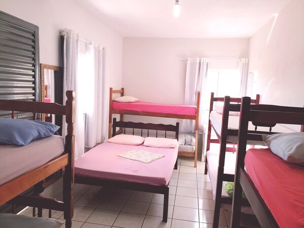 A dormitory room with bunk beds, a wooden headboard, a mirror, and a window with curtains.