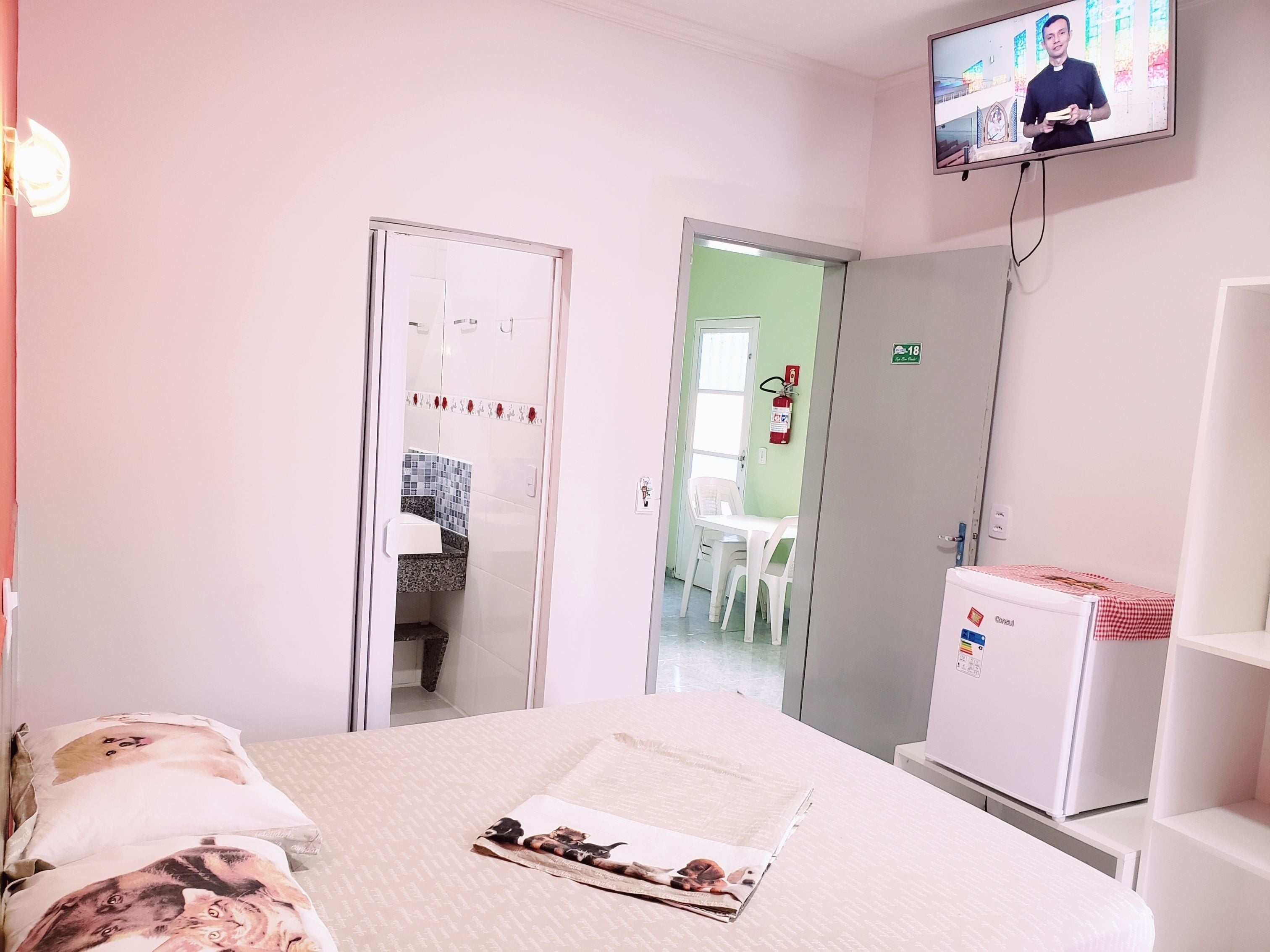 Una habitación de hotel con cama, televisor, refrigerador pequeño y una puerta que da a un baño.