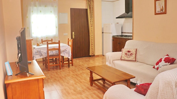 A living room with a sofa, a wooden coffee table, a TV on a stand, a dining table with chairs, and a kitchen area with a stove and cabinets. - Two bedroom apartment close to beaches (Conil de la Frontera)