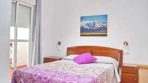 A bedroom with a bed, a nightstand, a wall-mounted lamp, and a window with curtains. - Two bedroom apartment close to beaches (Conil de la Frontera)