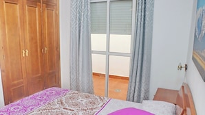 A bedroom with a bed, a wooden wardrobe, a balcony with a view, and a painting on the wall. - Two bedroom apartment close to beaches (Conil de la Frontera)