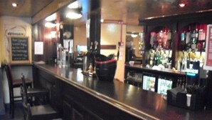 Een bar met een toonbank, stoelen en diverse flessen.
