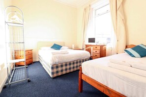 A hotel room with two beds, a wooden dresser, a desk with a computer, a metal rack with hangers, and a window with curtains.